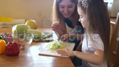 女儿和妈妈在厨房。 一个女孩帮她妈妈准备沙拉。 一个女人尝<strong>试卷</strong>心菜。 素食绿色