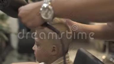 发型师在理发店用烘干机做男孩发型。 <strong>儿童美发</strong>沙龙晾晒头发.. 美容师