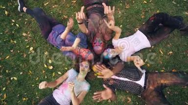 镜头放大了躺在草地上的放松的多民族人群，他们有着五颜六色的脸和衣服，看着镜头