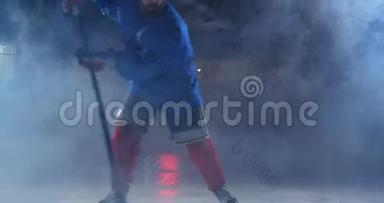职业冰球运动员带着棍子和冰球在鲁达身上移动，穿着溜冰鞋和头盔在黑暗的背景和烟雾中移动
