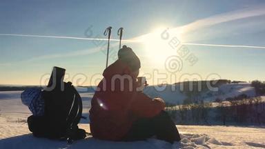 人类旅行者坐在冬天的山上的悬崖上，<strong>喝热水</strong>瓶里的茶。 年轻人的后景