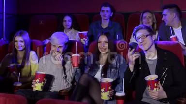 年轻的朋友坐在<strong>电影院</strong>里喝着<strong>爆米花</strong>和饮料，看一部喜剧电影。