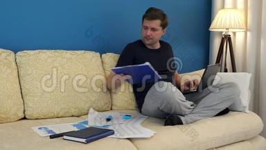 男人坐在沙发上，用笔记本电脑和财务图表工作。 小生意。