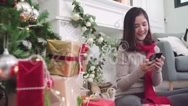 快乐的年轻亚洲女人在圣诞<strong>节</strong>期间，用智能<strong>手机</strong>在家里的客厅里查看社交媒体。