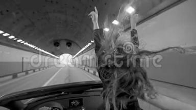 一个漂亮的年轻女孩坐在隧道里的一辆红色敞篷车里。 公路上的路。 穿着皮夹克。 头发