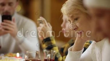 在节日圣诞晚餐期间，祖母与其他家庭成员一起在智能手机上上网，亲密无间。