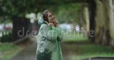 漂亮的年轻女人在<strong>下雨</strong>天在公园里跳舞，听着耳机里的<strong>音</strong>乐，穿着雨衣。