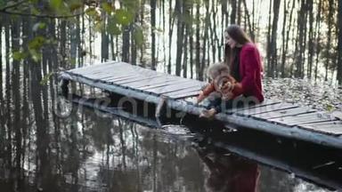 母子俩坐在湖边的一座木桥上，欣赏美丽的景色.. 家庭的概念