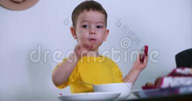 小可爱的孩子坐在桌子旁吃自己的燕麦片，吃异国情调的水果，宝宝心甘情愿地吃。 概念
