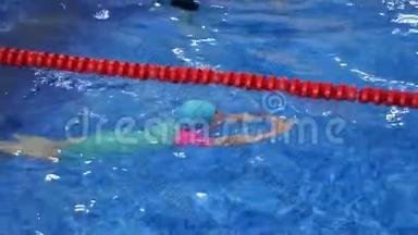 戴着护目镜、泳衣帽和脚蹼的小女孩正在游泳池里训练游泳。