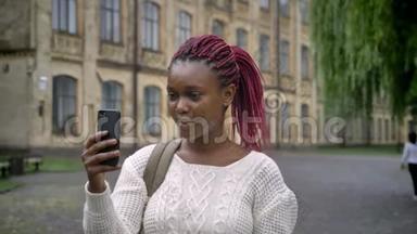 一个年轻的非洲<strong>学生</strong>，带着粉红色的长发，通过智能手机进行视频<strong>聊天</strong>，谈笑风生，快乐的女人