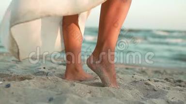 一个穿着白色长裙的白种人女孩的腿站在<strong>蔚蓝</strong>的<strong>大海</strong>的岸边，站在沙滩上，太阳，镜头.. 慢慢