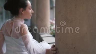 美丽的新娘，穿着优雅、奢华的象牙色连衣裙的发型，摆在柱子附近