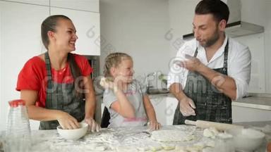 快乐的父母和女儿一起在厨房里快乐。 年轻的父母正在教他们的女孩如何做饭。