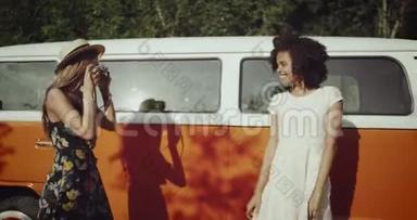 在老式橙色巴士旁边，有两个非洲女孩和金发女孩，从老式照片相机拍照