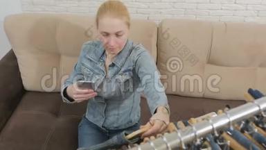 一个女人坐在沙发上，用一部智能手机检查和拍照，这是一套挂在沙发上的牛仔服装
