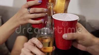 目标特写镜头欢呼与瓶饮料和红色塑料杯。 朋友们聚在一起，聚在一起