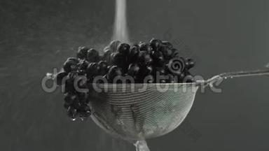 在视频中，我们看到葡萄在筛子中，水在喷射中从顶部落下，然后随着水滴停止，灰色的背景
