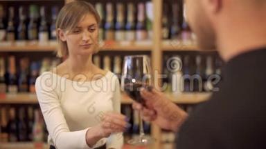 酒铺里的女孩给男人提供一杯酒。 一位到酒类商店的客人拿着一杯葡萄酒和