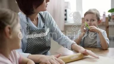 <strong>妈妈</strong>一边给孩子们<strong>讲故事</strong>，一边在厨房的桌子上擀面包做饼干