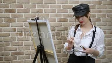 戴皮帽的女艺术家在画布上靠砖<strong>墙画</strong>一幅画