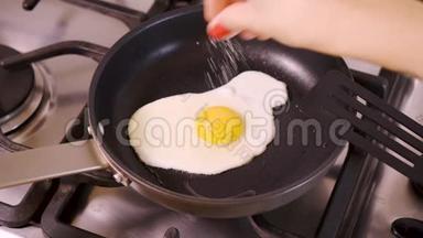 女人在家厨房炒鸡蛋，在平底锅里加盐吃煤气灶