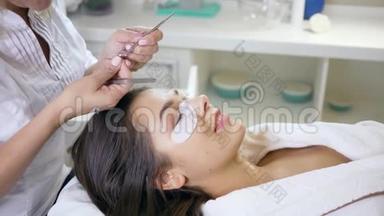 美容院的工作人员用镊子将睫毛粘在睫毛上，女工在睫毛过程中用眼贴