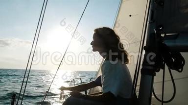 快乐的年轻女子穿着礼服，坐在桅杆旁的甲板上，日落时<strong>扬帆</strong>远航