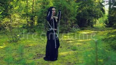 一个穿着黑色衣服的年轻女巫从锁链上挣脱出来，在森林的空地上和他们一起旋转。 万圣节。 哥迪克风格。