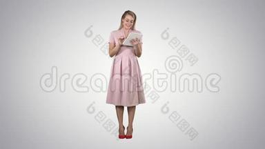 漂亮的年轻女人穿着粉<strong>红色</strong>的连衣裙，拿着平板电脑，在<strong>渐变</strong>的背景下看着它。