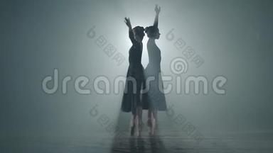 两个优雅的职业芭蕾舞演员在她的尖角芭蕾<strong>舞鞋</strong>上跳舞，在演播室的黑色背景上聚光灯下