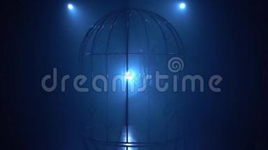 一个女孩在笼子里的舞台上抱箍旋转的剪影。 蓝色烟雾背景。 慢动作