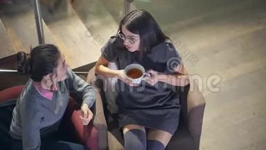 两个浅黑肤色的年轻女孩坐在椅子上一边聊天一边喝茶