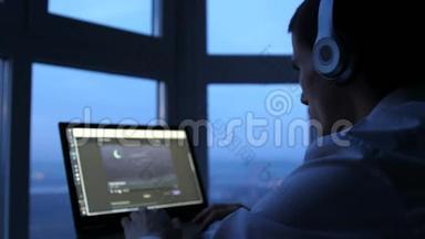 戴耳机的年轻人晚上在全景窗口使用平板观看<strong>电影</strong>。 3840x2160，4k