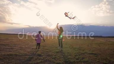 幸福的家庭母女在日落时分在草地上放风筝。 有趣的家庭时光。 友好家庭的概念