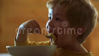 宝宝吃。 可爱的孩子在家吃早餐。 可爱的笑着的金发小男孩的肖像