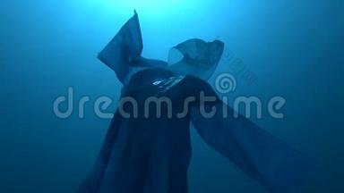 蓝色塑料雨衣作为幽灵慢慢漂浮在蓝色的水中。 海底塑料污染海洋