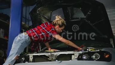 可爱的金发女孩修理<strong>汽车</strong>，并在服务站的<strong>汽车</strong>罩下用帮助扳手固定发动机的细<strong>节</strong>