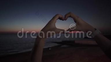 140女孩用她的手做一个心脏标志。 海边浪漫的夜晚.. 爱上了日落。 浪漫浪漫