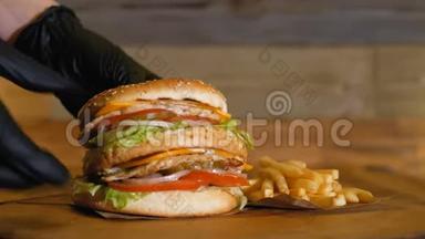 黑色手套在薯条旁边的木板上放了一个多汁的汉堡，上面有两个小切和蔬菜。 不健康