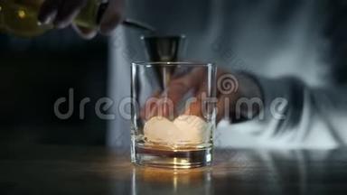 酒保把威士忌倒在酒杯上，然后倒在加冰的玻璃杯上，在酒吧里调制酒和鸡尾酒