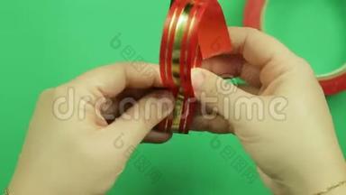 女人`手包一条红色丝带，用于在模板上做礼物蝴蝶结。 绿色背景