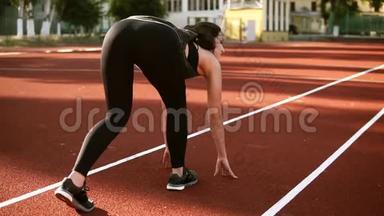 女运动员开始在跑道上跑步。 穿着黑色紧身裤的运动型黑发女人在跑道上慢跑
