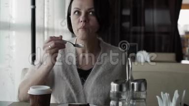美丽的黑发女人从杯子里喝咖啡，吃奶酪蛋糕