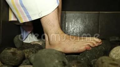 桑拿浴室里的热石头和一桶水特写男人`脚。