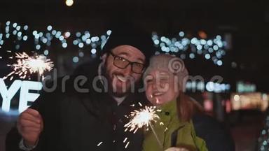 幸福的夫妻，夫妻在街上庆祝新年。 他们手里拿着火花，对着
