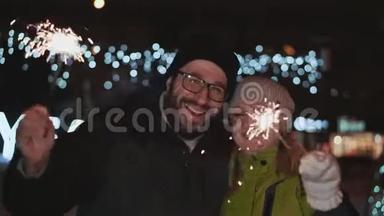 幸福的一对，夫妻庆祝新年。 冬天在外面。 他们手里拿着火花，对着
