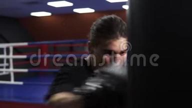拳击手打拳击梨。 一个愤怒的拳击手戴着黑色手套在拳击袋里打了一拳。 在健身房锻炼