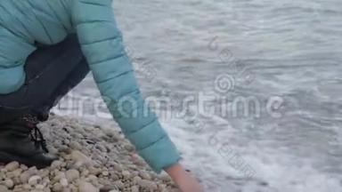 孤独寒冷海滩的女人。 一位迷人的白种人女子在海滩上水边玩石头。