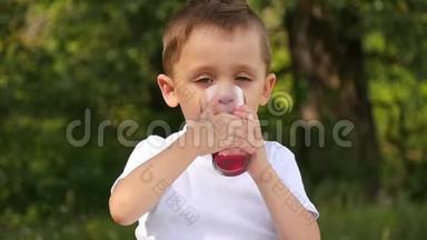 孩子在大自然中喝红果汁.. 一个小男孩喝着果汁，把杯子放在桌子上微笑着。 婴儿<strong>节目</strong>
